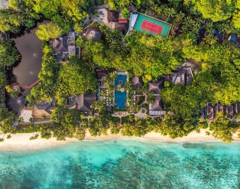 Aerial view of Niva Labriz Resort with beach, pool, tennis court, and lush greenery.