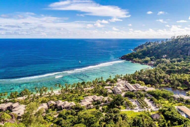 Aerial view of Kempinski Seychelles Resort with lush greenery and ocean coastline.