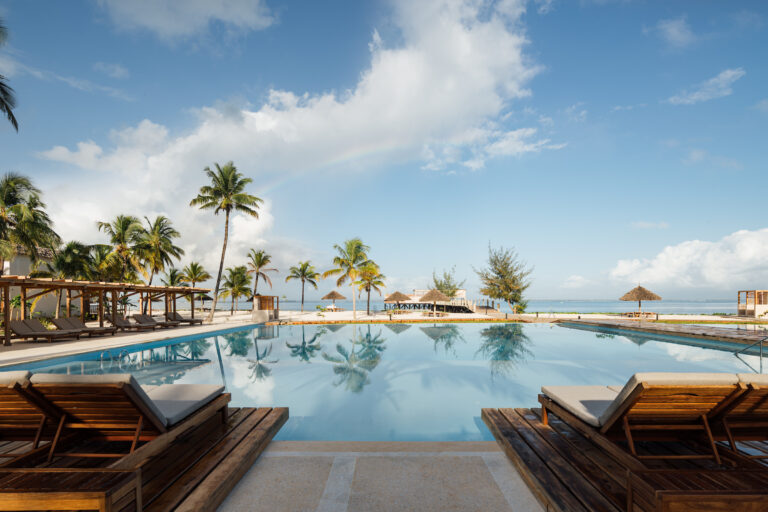 Luxury poolside scene at JAZ Elite Aurora with palm trees and ocean view.